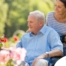 A caregiver brings an older adult with a wheelchair to see some flowers representing how professional caregivers can make outdoor activities accessible.