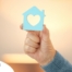 A hand holds up a cutout of a home with a heart in it, representing the home care industry.