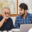 A man looks at a computer with his father who is confused, representing one of the early signs of dementia.