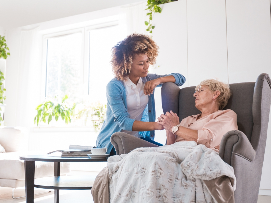 Home Care in Ocean Ridge Caregiver providing compassionate home care in Ocean Ridge, holding hands with an elderly woman in a comfortable living room setting, offering support and reassurance.
